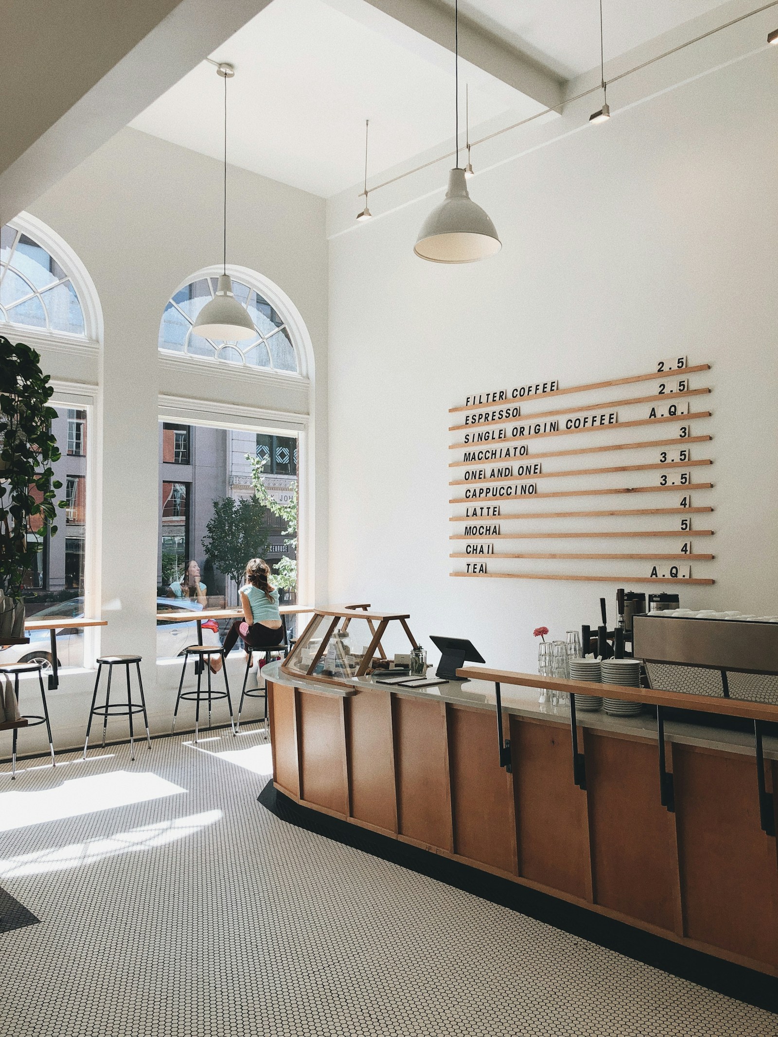 A bright cafe with a wooden counter, arched windows and small tables.