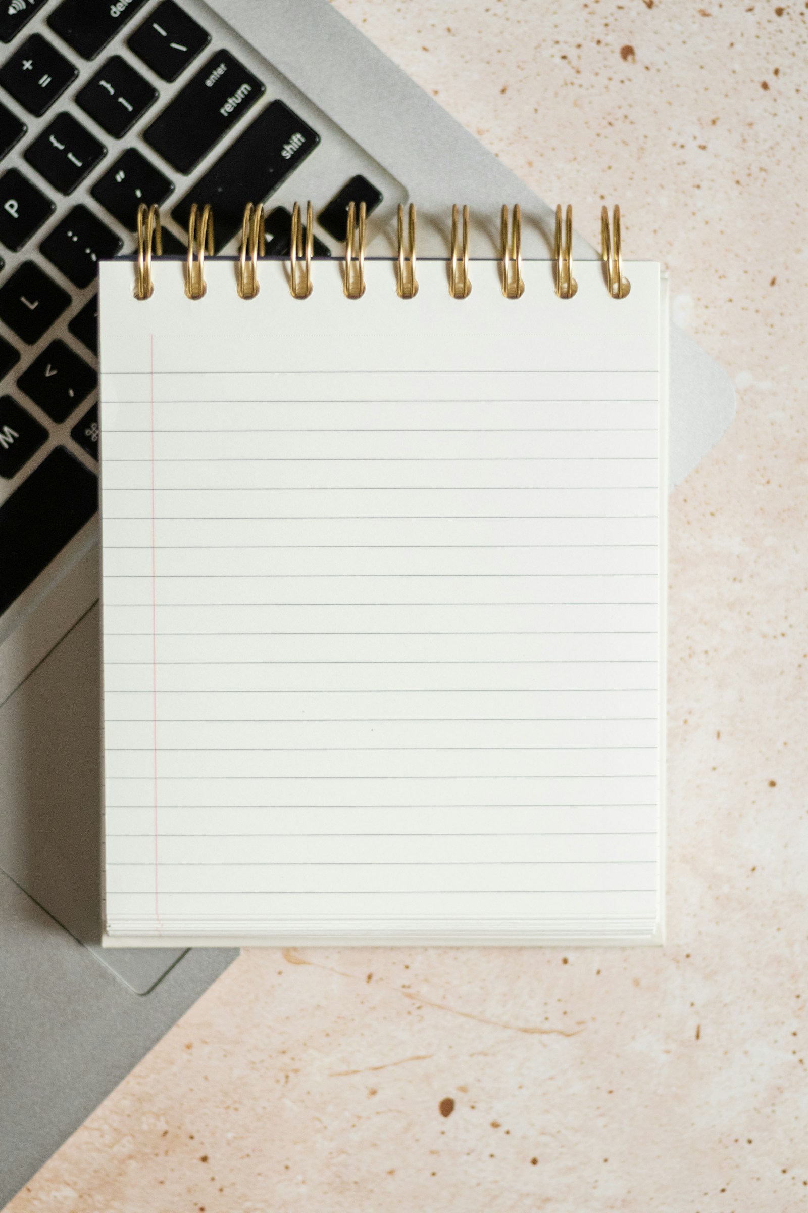 A lined spiral notebook beside the corner of a laptop.