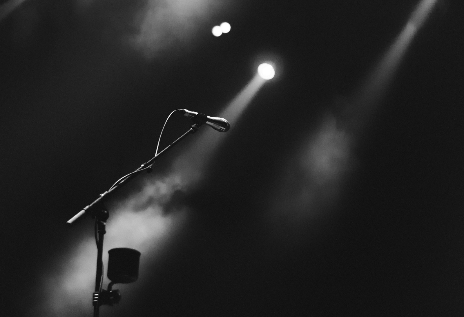 A microphone silhouetted under a spotlight on a dark stage.