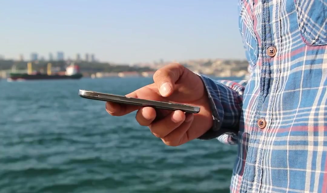 Close-up of a hand holding a smartphone by the water