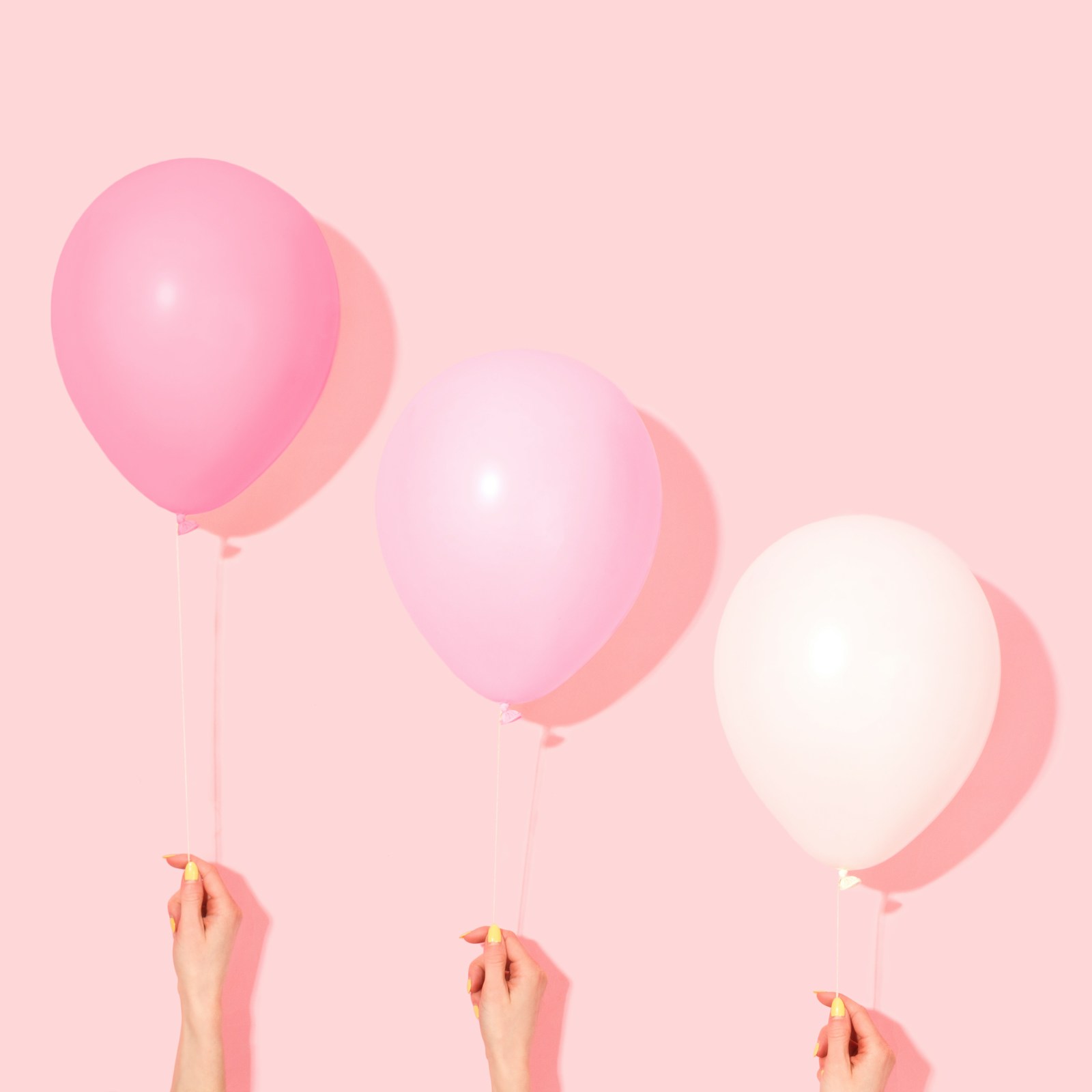 Hands holding pink and white balloons against a pink background.