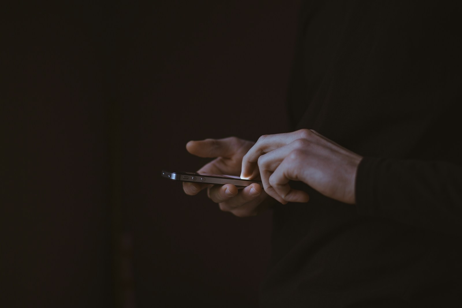 Hands using a phone in a dark, quiet setting.