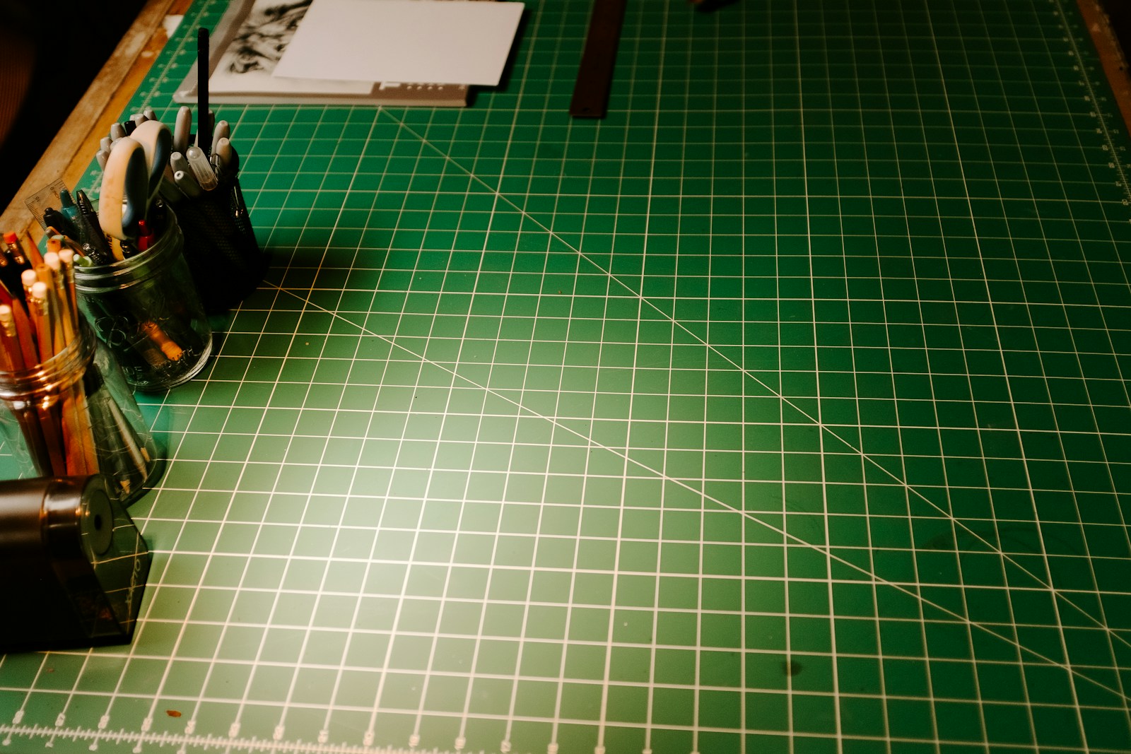 A green cutting mat with measurement lines and pencils at the edge.