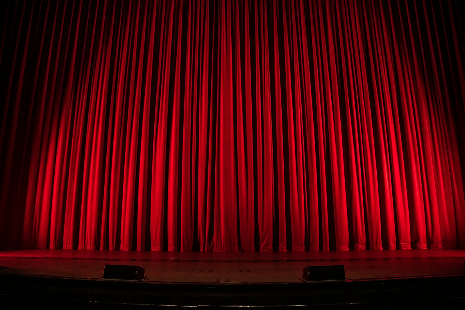 Closed red theater curtains under stage lights.