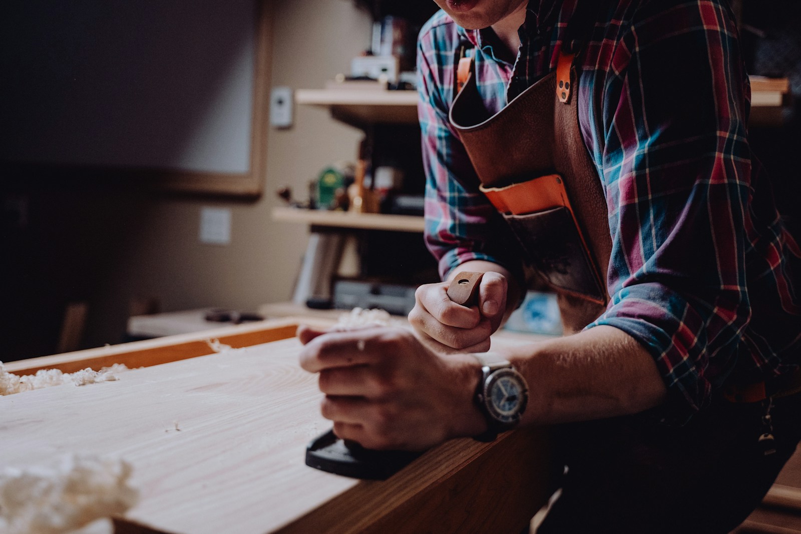 A craftsperson using a hand plane on wood at a bench, with their face outside the frame.