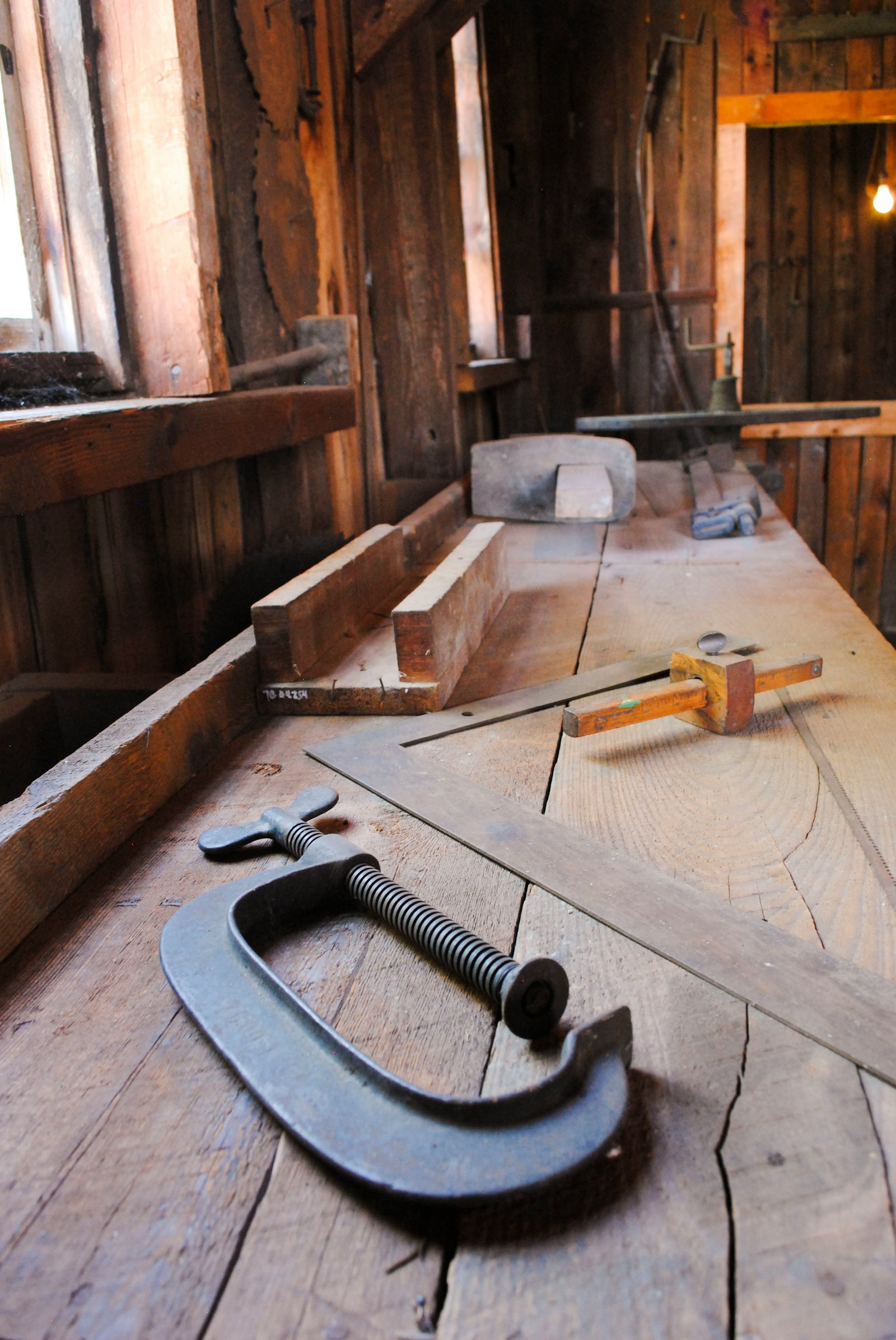 A clamp and woodworking tools on a sunlit workshop bench.