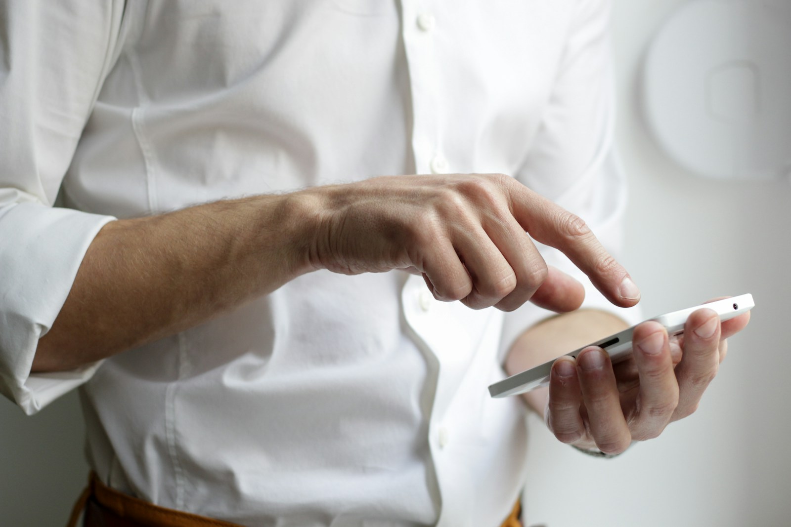 Hands tapping a smartphone against a plain white shirt.