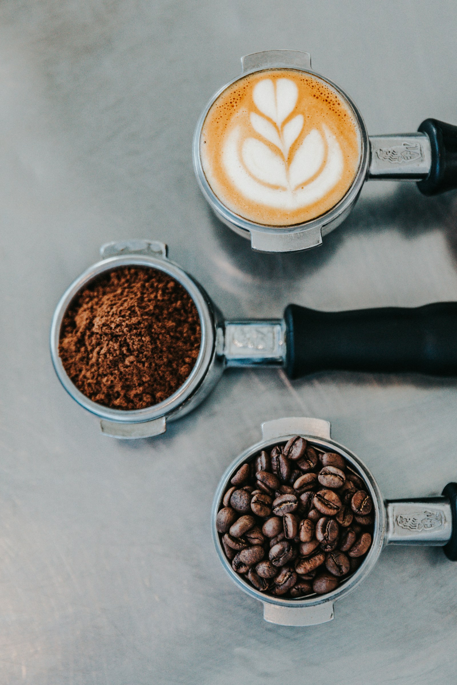 A finished coffee beside ground coffee and beans on a work surface.