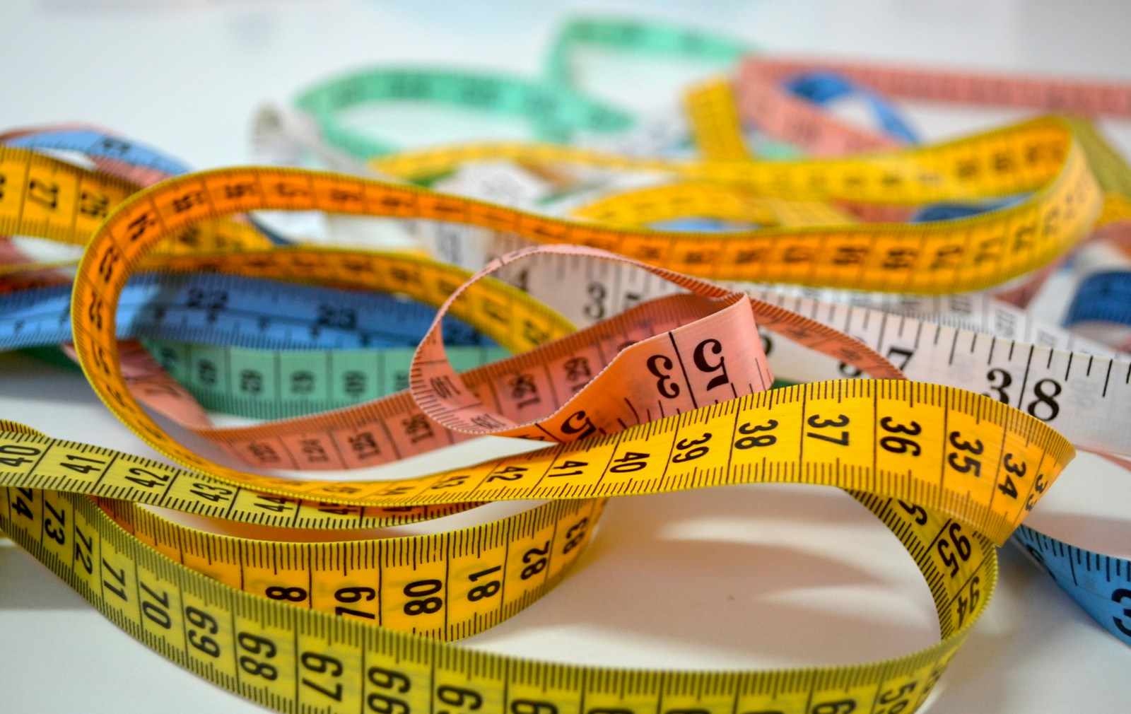 Several colorful flexible measuring tapes tangled on a light surface.