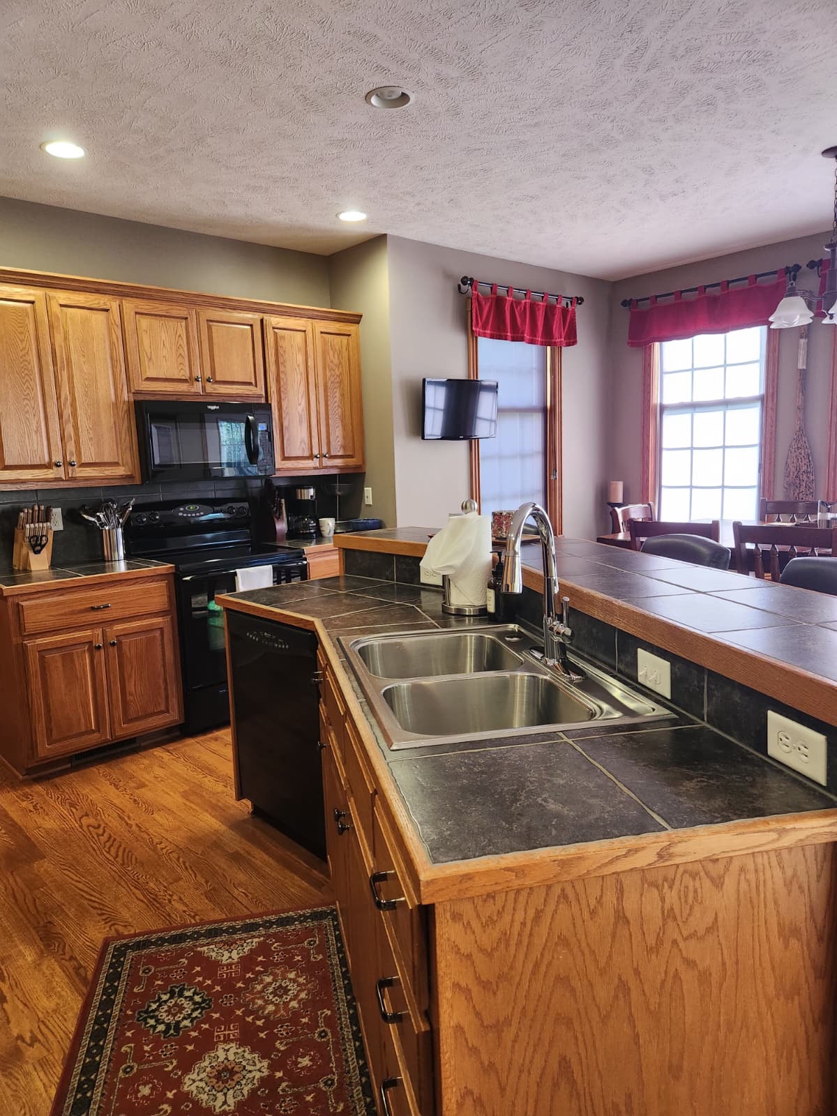Kitchen overview with oak cabinets, tile counters, double sink and adjacent dining area