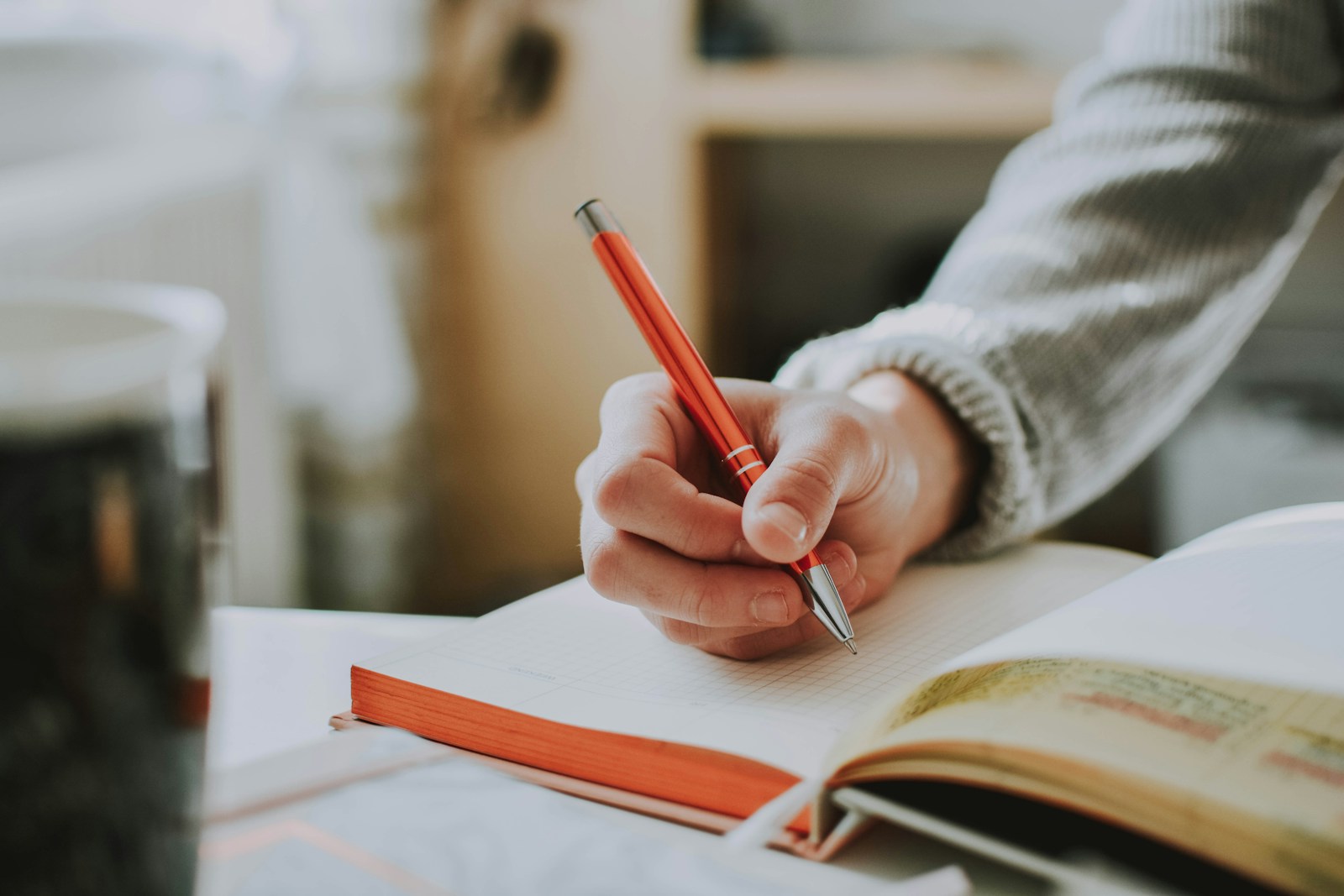 A hand holding a pencil above an open notebook.