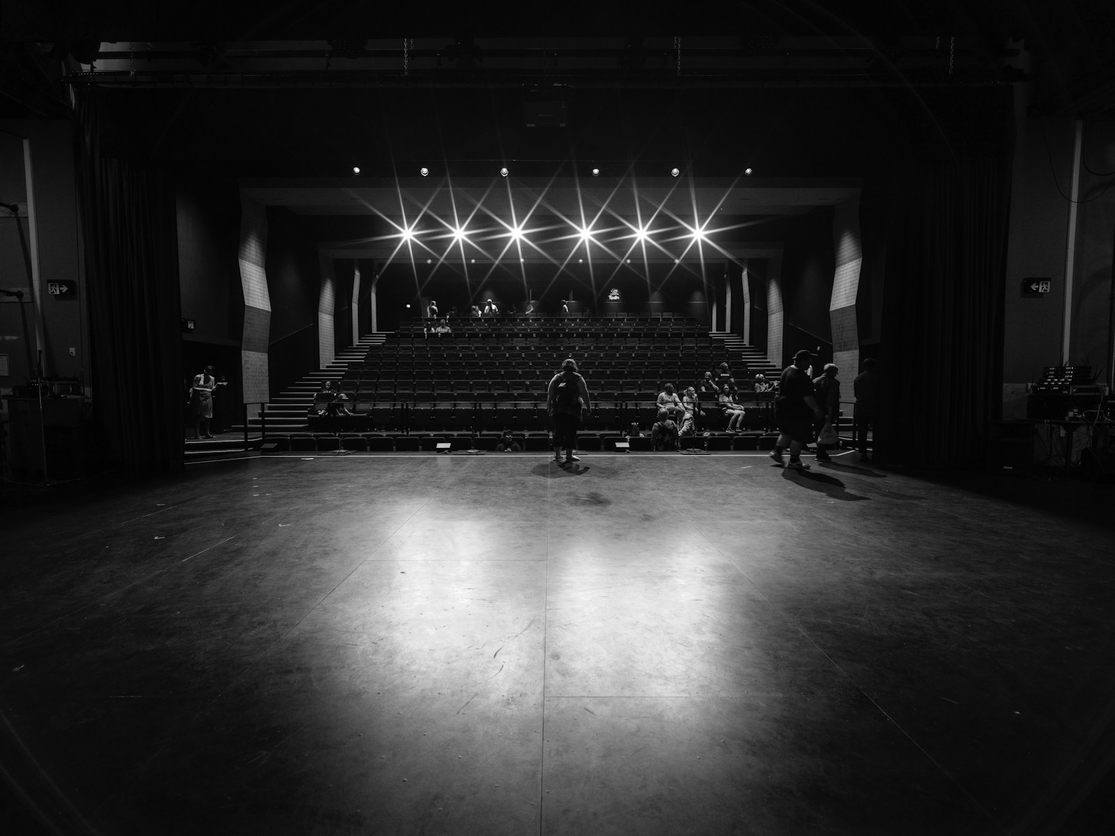 An empty theater stage seen toward rows of seats and bright lights.