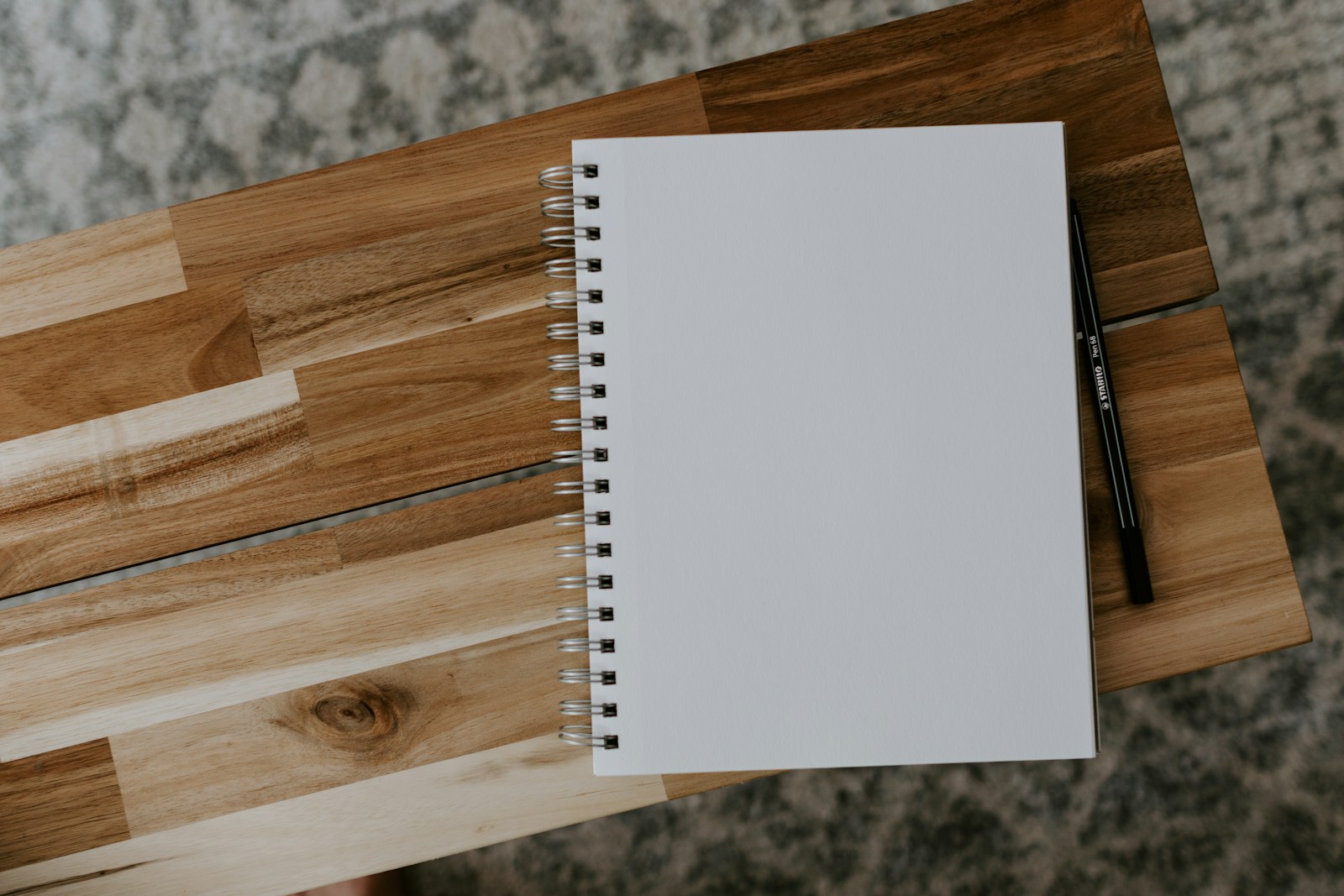 A plain spiral notebook and black pen on a wooden table.