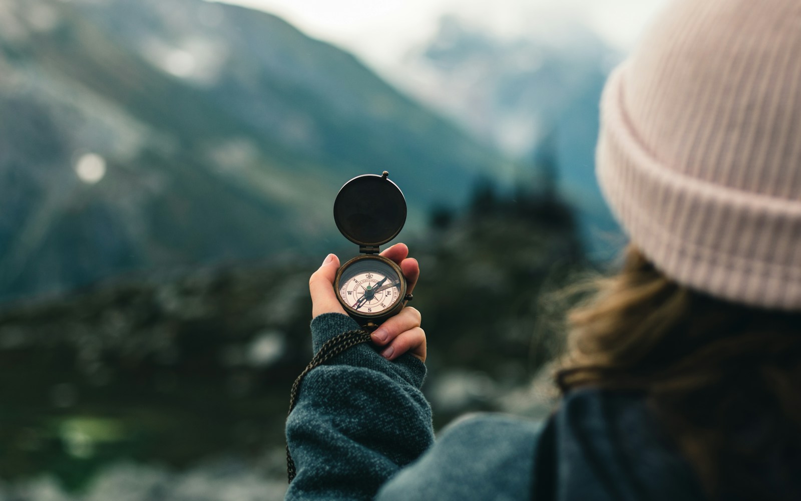 A person seen from behind holding a compass toward a mountain landscape.