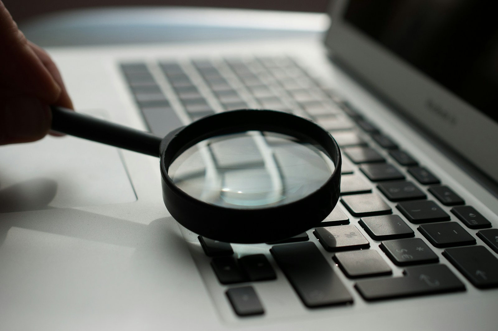 A magnifying glass held above a laptop keyboard.