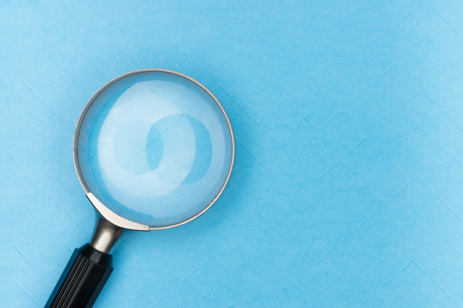 A magnifying glass on pale blue paper.