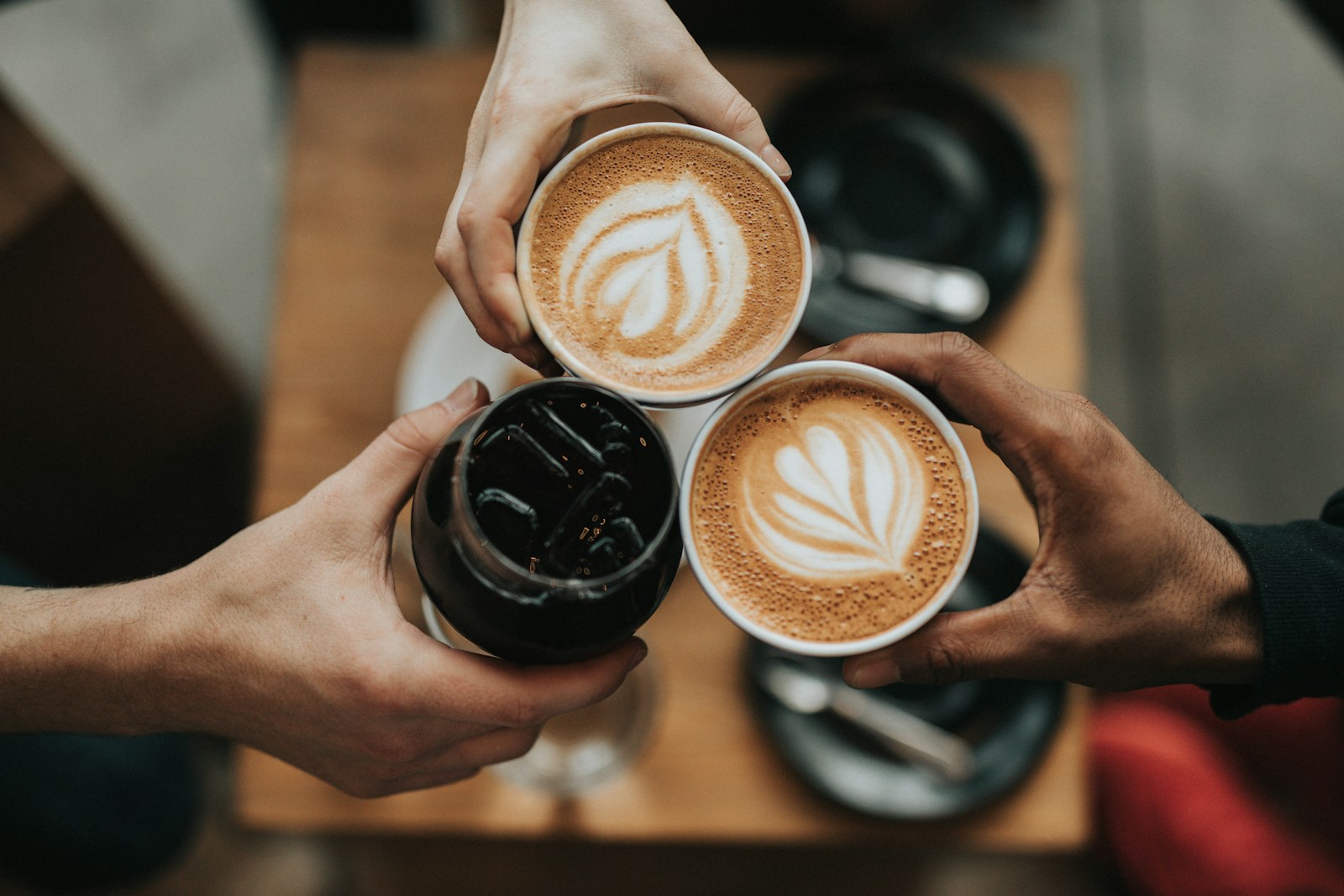 Three people holding cups of coffee together, with only their hands visible.