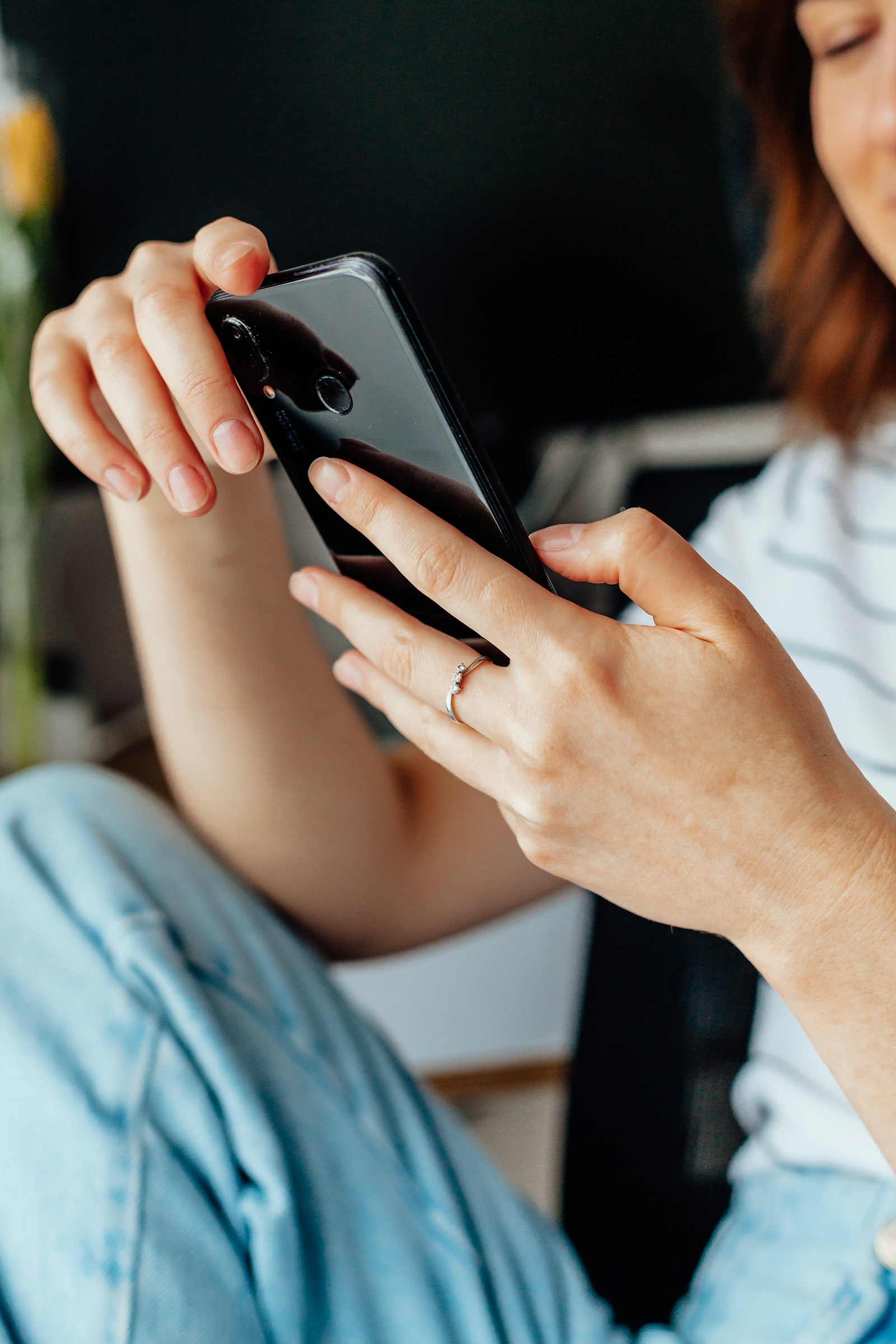 Hands using a smartphone while seated, with the face mostly outside the frame.