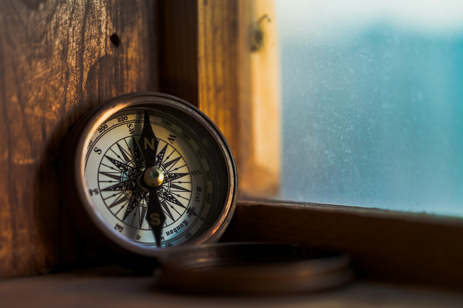 A brass compass resting against a wooden window frame.