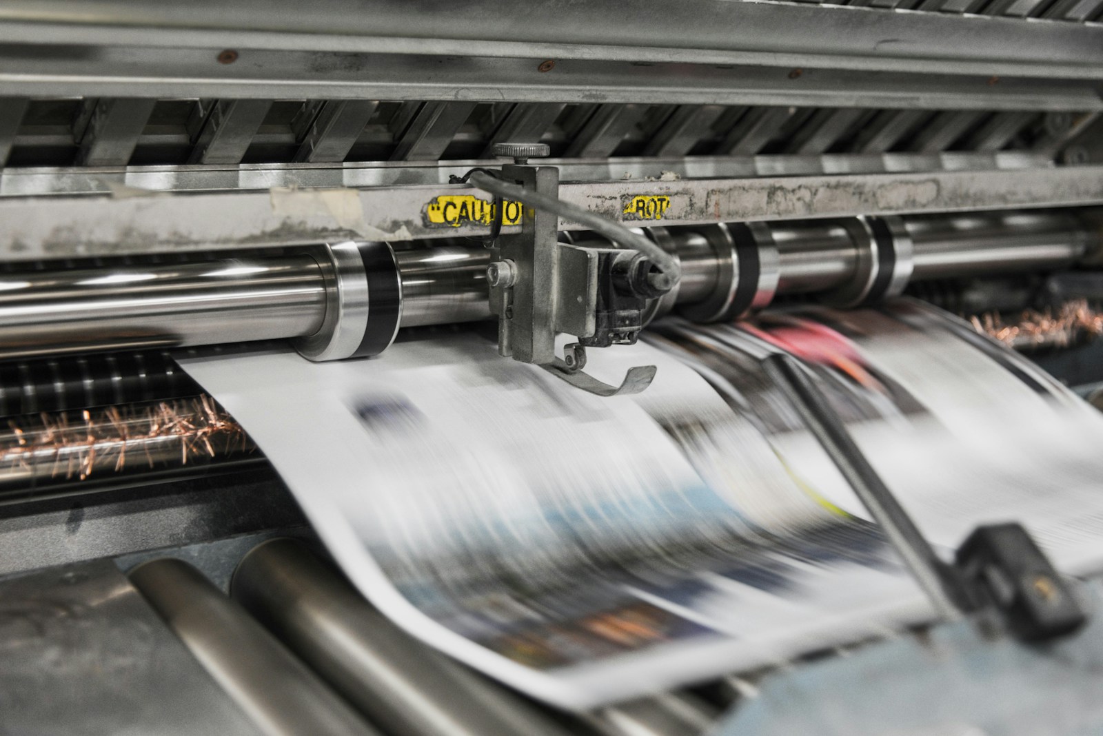 Paper moving through the rollers of a printing press.