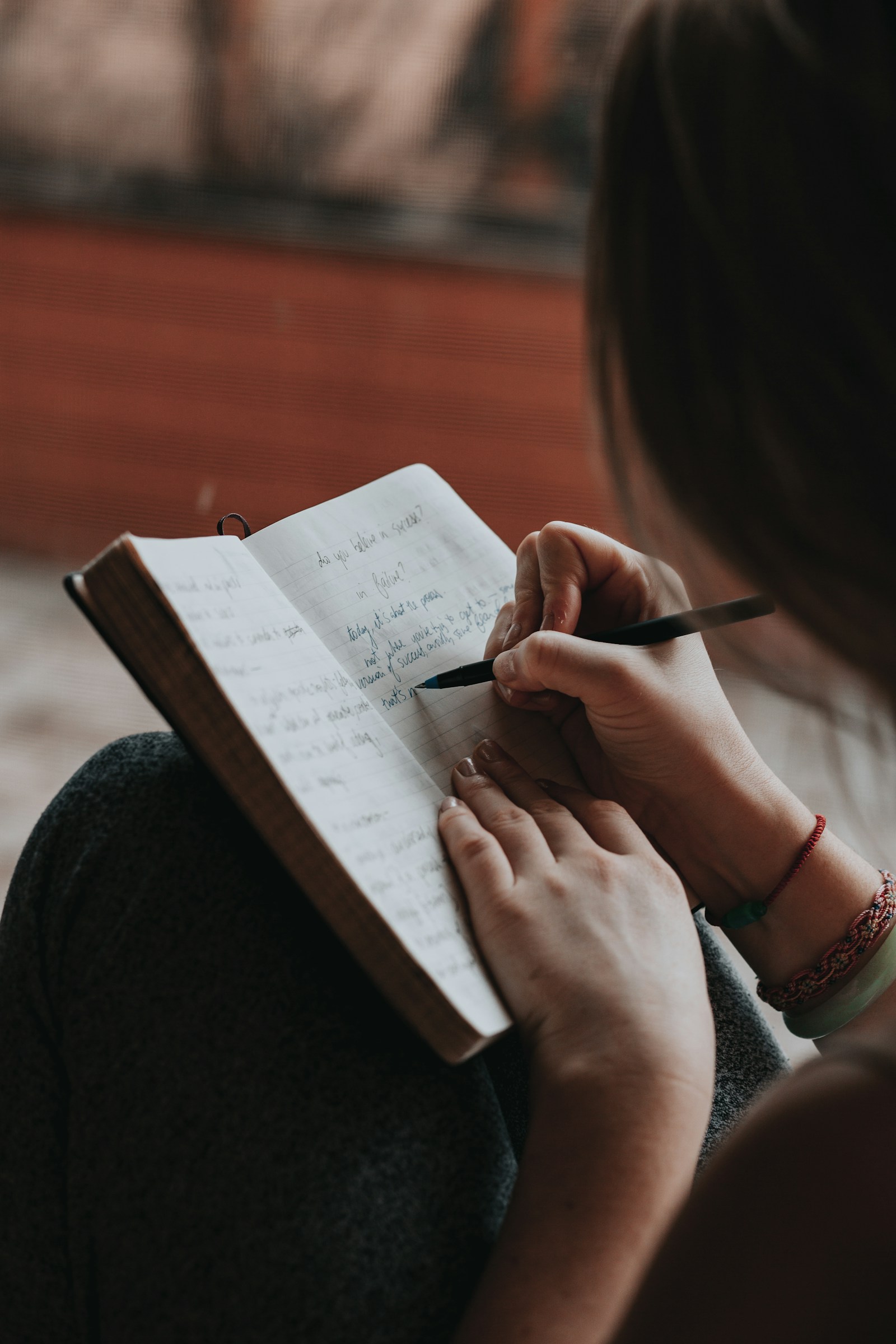 A person writing in a small notebook resting on their lap.