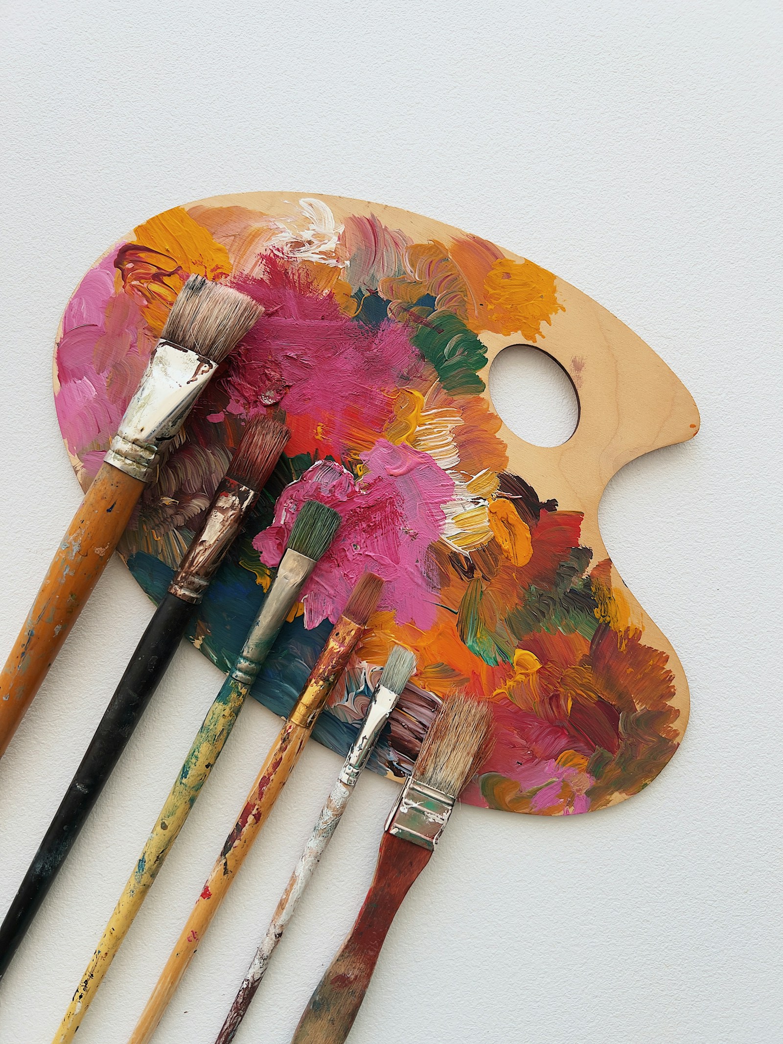 A well-used artist’s palette and several paintbrushes on a white background.