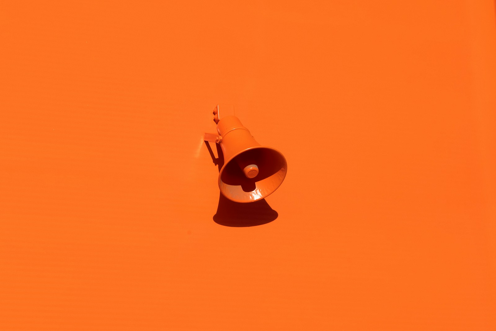An orange megaphone suspended against an orange background.