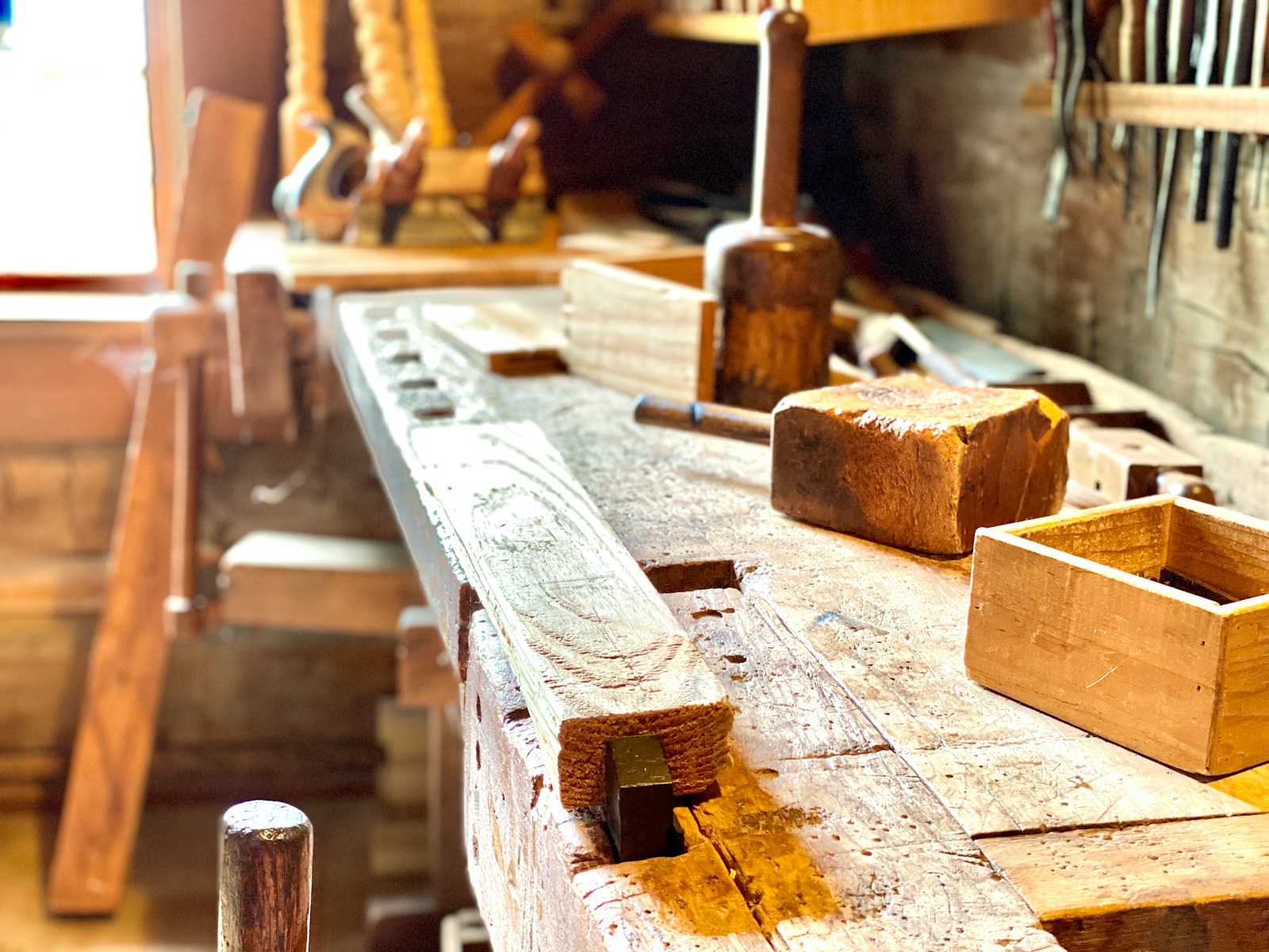 Wooden hand tools and a small wooden box on a sunlit carpenter's workbench.