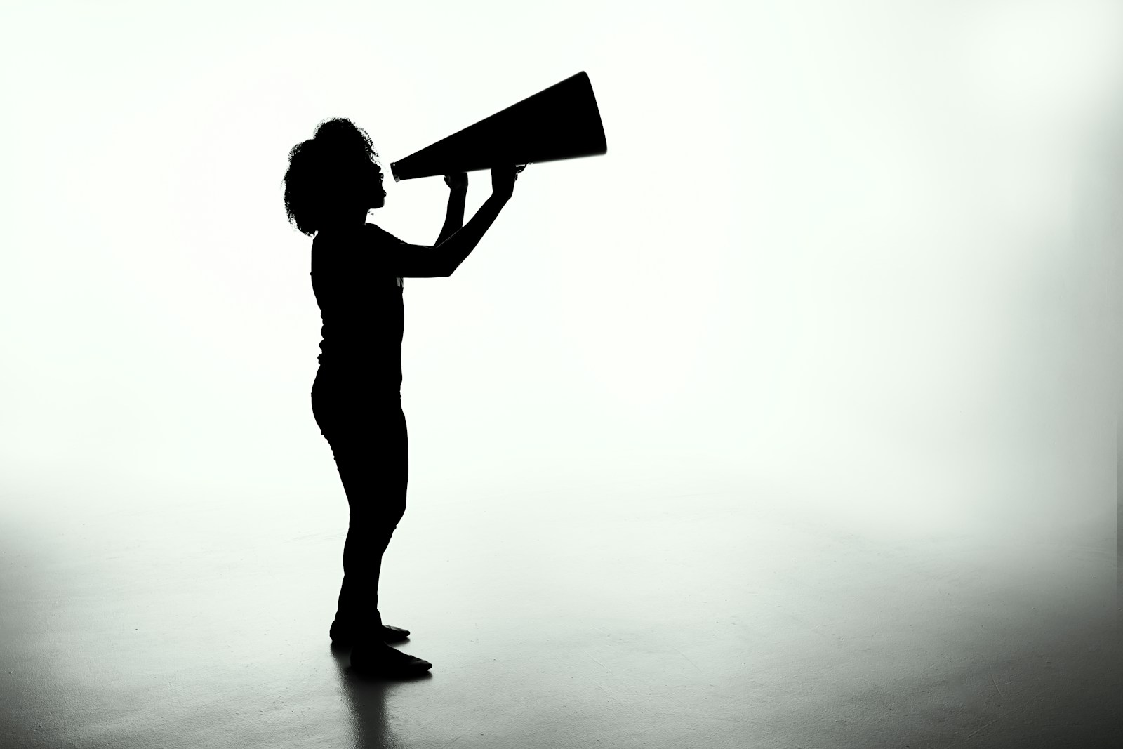 A silhouette holding a large megaphone against a light background.