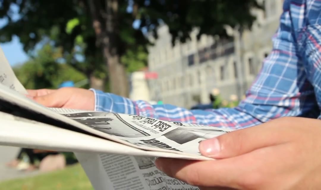 Person reading the newspaper in a park outdoors