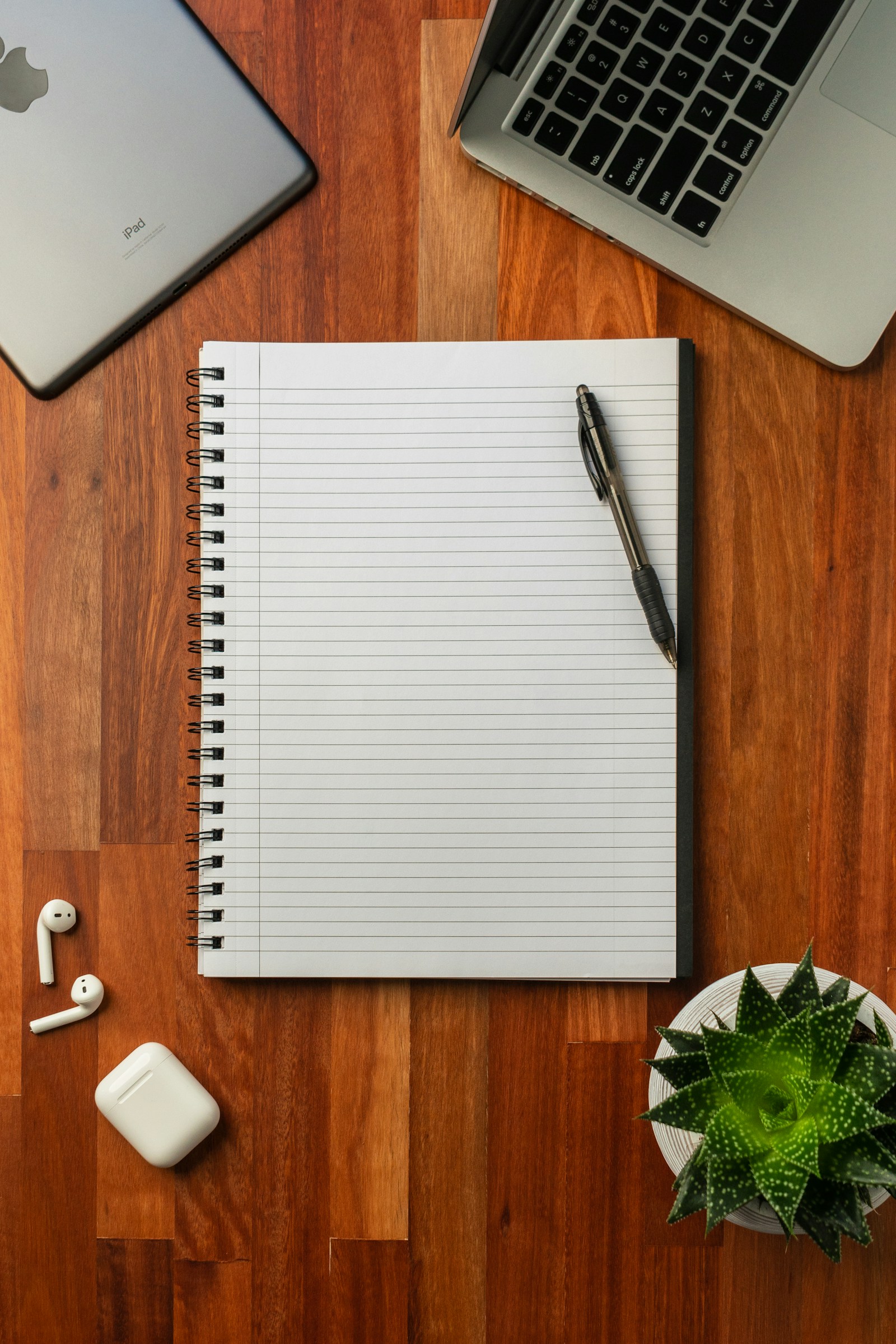 A paper notebook beside a laptop on a wooden desk.
