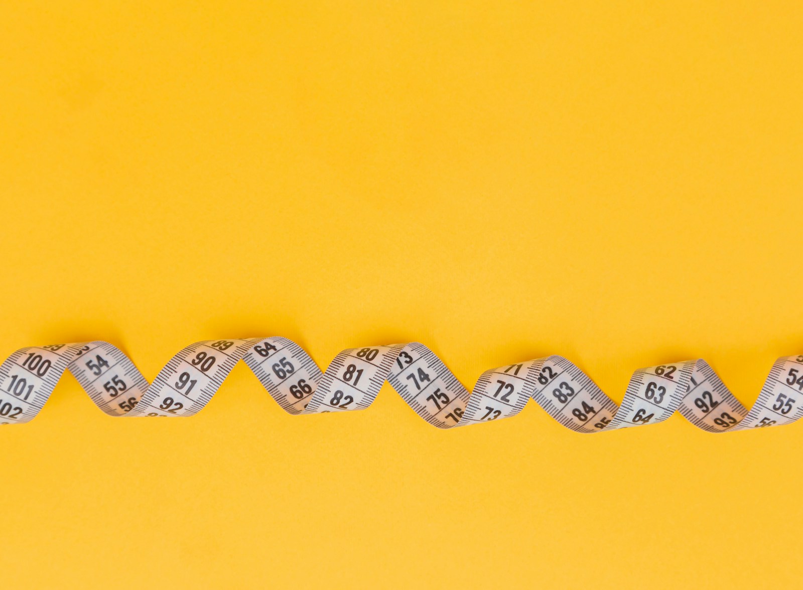 A white measuring tape arranged in a wave on a yellow background.